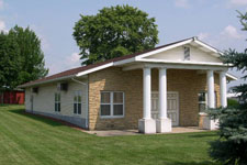 image of a small building with columns and a portico on a sunny day, blue sky, green grass.